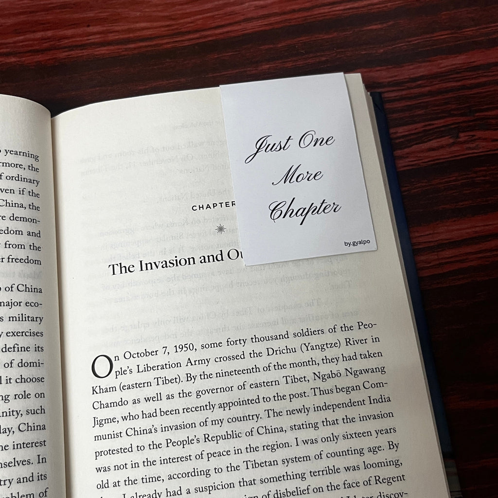 Open book with a magnetic bookmark labeled 'Just One More Chapter' on a wooden surface