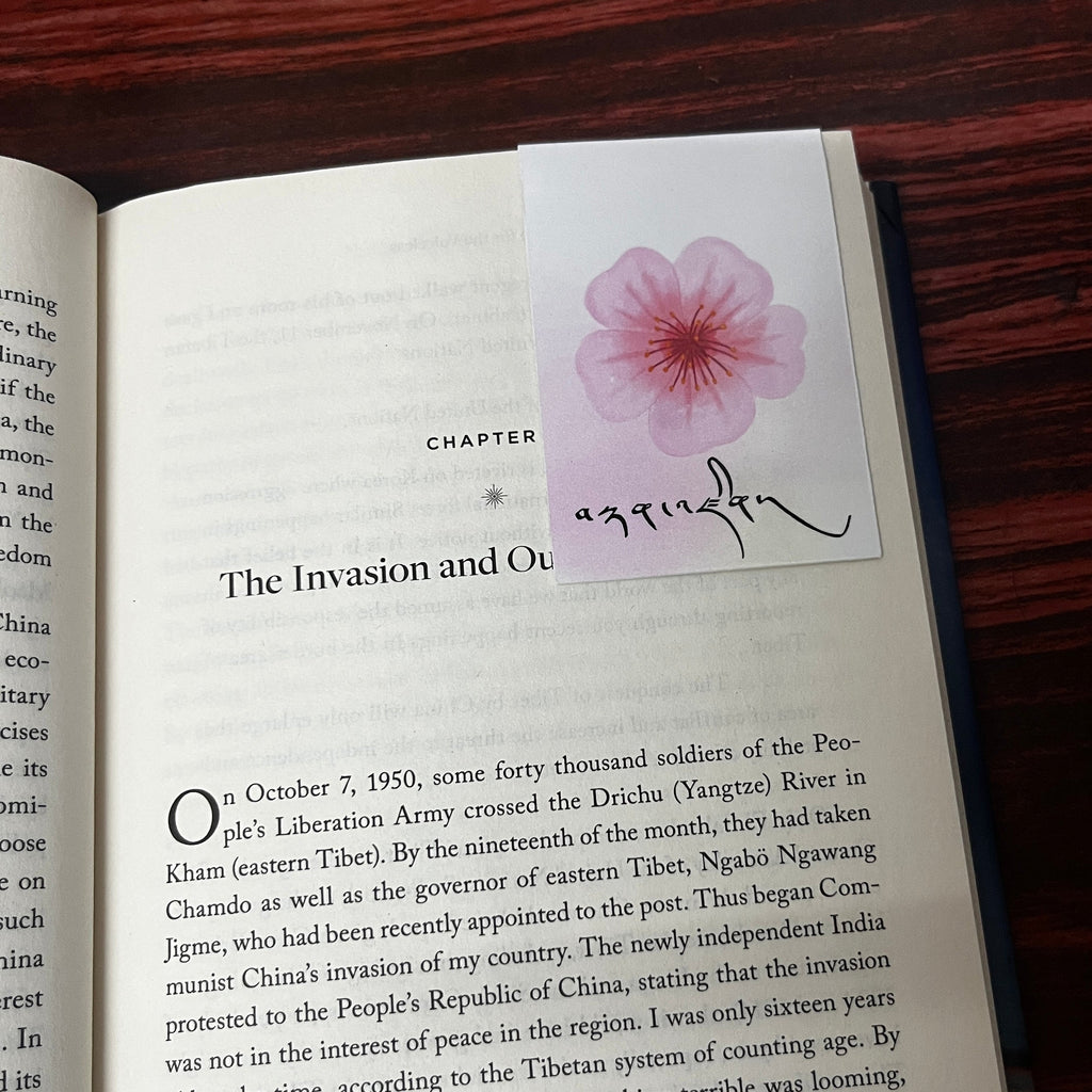 Open book with a bookmark featuring a pink flower design with the tibetan name Tenzin on a wooden surface