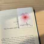 Open book with a bookmark featuring a pink flower design with the tibetan name Tenzin on a wooden surface