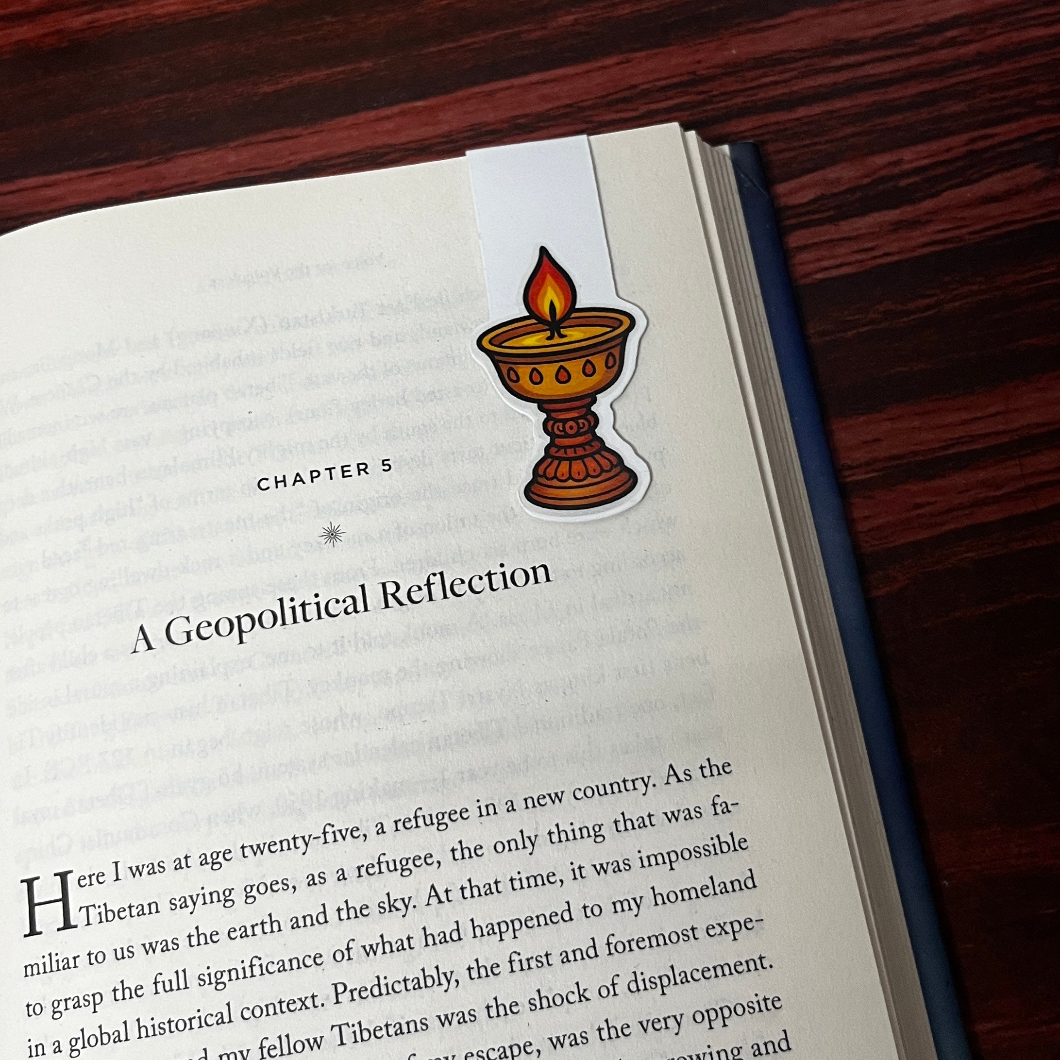 Book with a bookmark featuring an illustration of a butter lamp on a wooden surface
